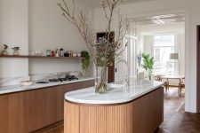 a beautiful and chic kitchen with a refined herringbone floor, light-stained cabinets, a curved kitchen island and an open shelf