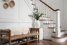 a beautiful and welcoming creamy entryway with white molded walls and a dark herringbone floor, a woven bench and some baskets