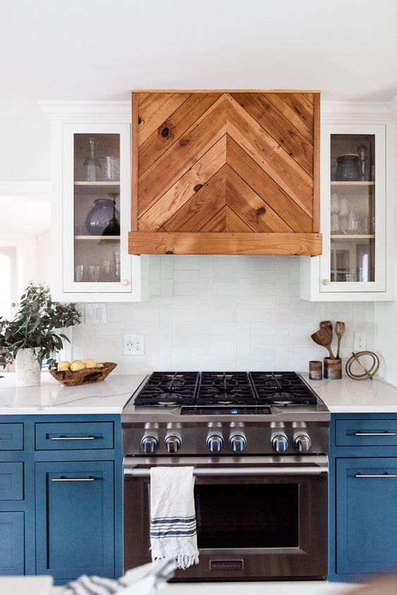 a beautiful blue and white kitchen with shaker cabinets, a pretty rich-stained chevron clad hood and white countertops