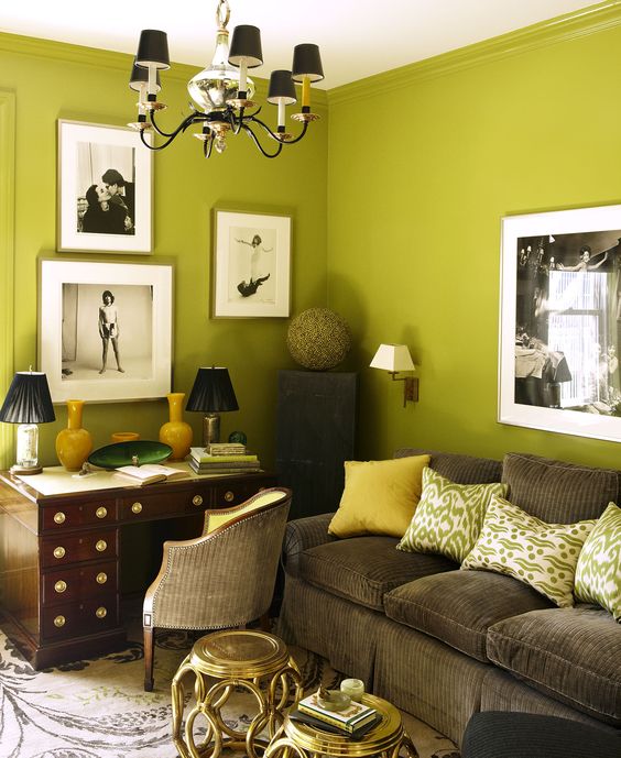 a beautiful chartreuse living room with a rich-stained desk, a brown velvet sofa, printed pillows, a gallery wall and a chandelier