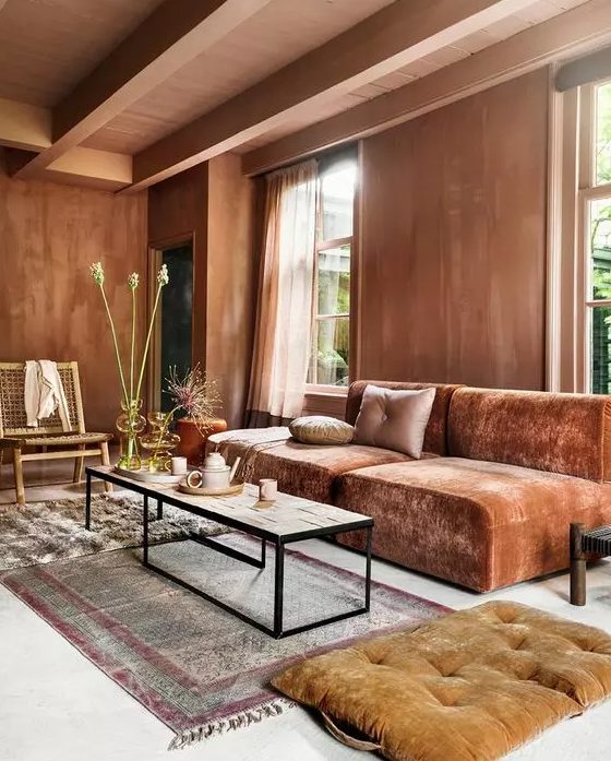 a beautiful living room with much texture, terracotta walls, a burnt orange low sofa, a coffee table and rust cushions