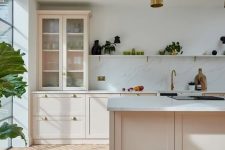 a beautiful modern peachy kitchen with terracotta herringbone tiles on the floor, a white stone backsplash and countertops and gold pendant lamps