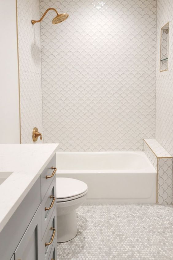 a beautiful neutral bathroom with white fishscale and pearl penny tiles, a grey vanity and gold fixtures is chic and cool