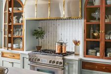 a beautiful refined kitchen with aqua cabinets, a white tile backsplash and a statement metal hood that matches the cooker