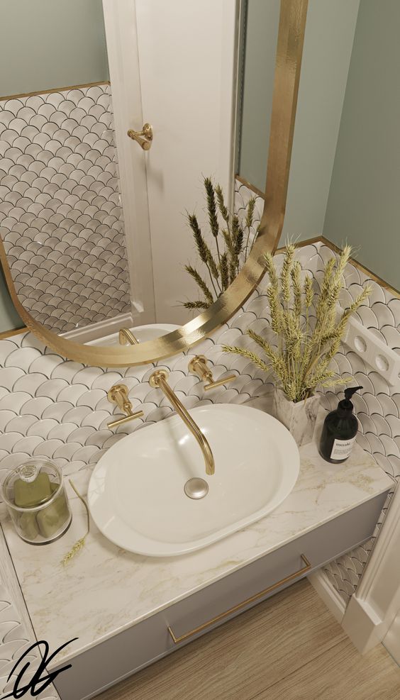a beautiful sink space with white scallop tiles, a marble vanity, a sink, an oval mirror and gold touches