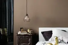 a bedroom with a brown accent wall, a bed with neutral bedding, a dark-stained nightstand, a pendant lamp