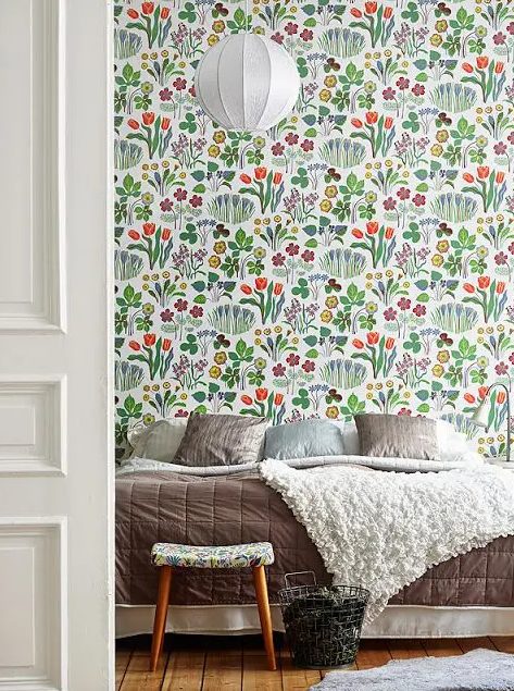 a bedroom with bright floral wallpaper, a bed with beige and neutral bedding, a stool and a paper pendant lamp