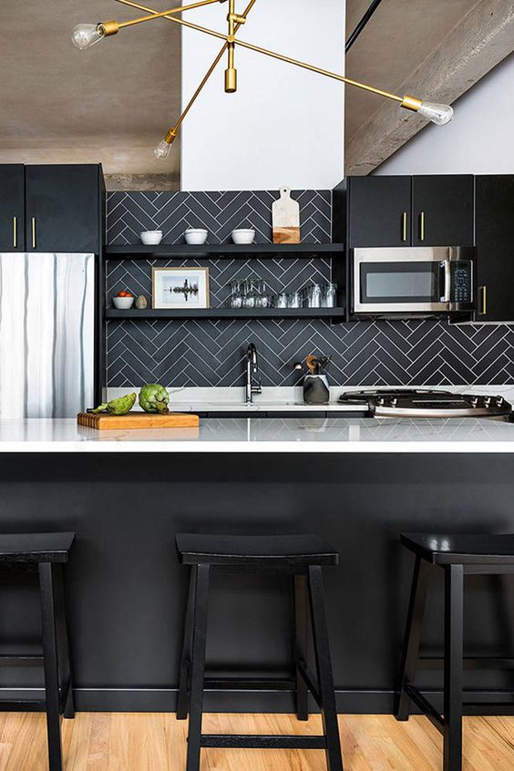a black and white kitchen with a black herringbone tile backsplash, a black kitchen island, white countertops and a gold chandelier