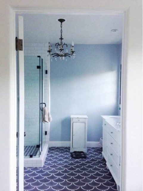 a blue and white bathroom with navy fishscale tiles on the floor, an elegant chandelier and white furniture looks sea-like
