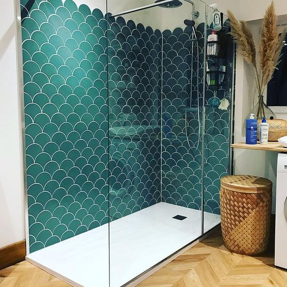 a boho bathroom done in neutrals, with a chevron floor and a shower space clad with green fishscale tiles, a basket and a sink