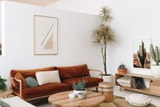 a boho living room with a rust-colored sofa, neutral furniture, a round table, simple textiles and potted plants