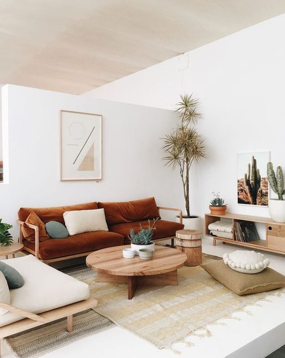 A boho living room with a rust colored sofa, neutral furniture, a round table, simple textiles and potted plants