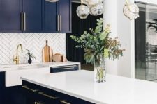 a bold and chic kitchen with navy cabinets, white countertops and a backsplash and a catchy chandelier with gold touches