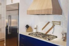 a bold blue kitchen with white stone countertops and a backsplash plus a stained wood hood looks amazing
