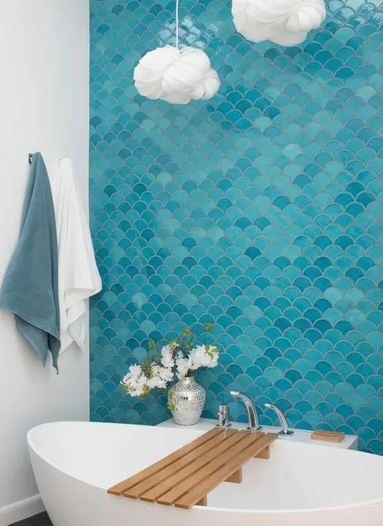 A bold modern bathroom inspired by the sea, with a blue and turquoise fish scale tile wall, an oval tub, cloud like pendant lamps
