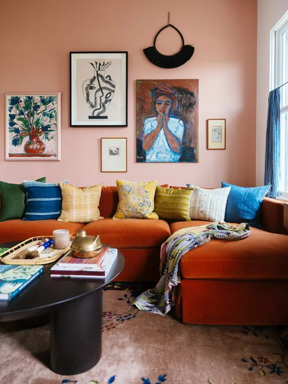 a bright living room with a Peach Fuzz accent wall, an orange sectional, colorful pillows, a gallery wall and a black coffee table