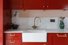 a bright red kitchen with a white stone backsplash and countertops, brass fixtures and some lovely decor
