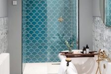 a bright seaside bathroom with turquoise fishscale tiles, a vintage clawfoot tub, a wooden mat and touches of gold