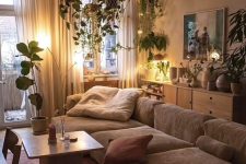 a calming earthy living room with a greige low sofa, a burgundy rug and pillows, a coffee table and lots of plants