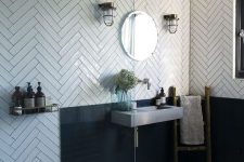 a catchy and chic bathroom with white herringbone tiles, a black backsplash, a concrete wall-mounted sink and vintage lamps
