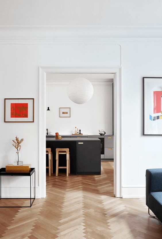 a catchy modern space with white walls and a neutral herringbone floor, dark furniture for a contrast, some bright artwork
