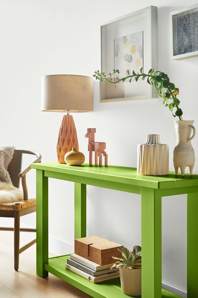 a catchy space with a chartreuse console table, elegant decor, some artwork, potted plants and a chair