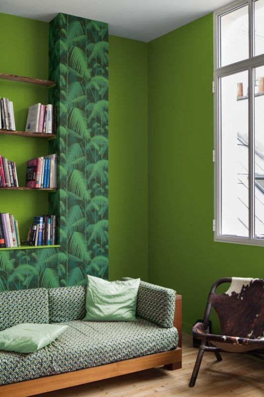 A chartreuse living room with a bold printed accent, shelves, a printed sofa and a chair with a cowhide