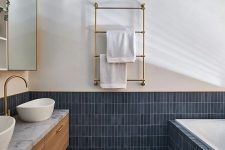 a chic modern bathroom done with navy stacked tiles and grey terrazzo, a sained vanity and gold fixtures