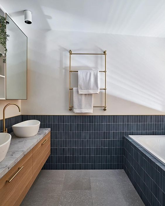 a chic modern bathroom done with navy stacked tiles and grey terrazzo, a sained vanity and gold fixtures