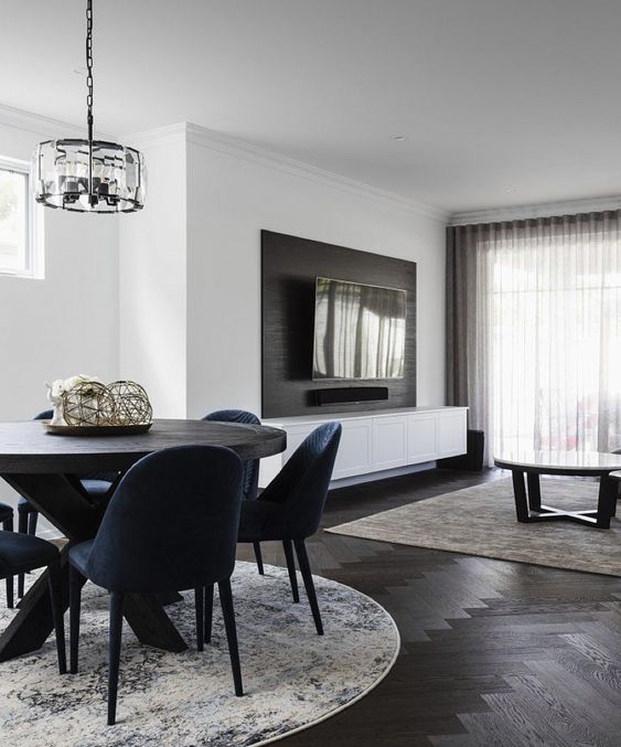 A chic modern space with white walls and a dark stained herringbone floor, a dark table and navy chairs, a coffee table