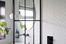a chic modern white bathroom with white herringbone tiles, a shower space, a vanity with a sink and black fixtures
