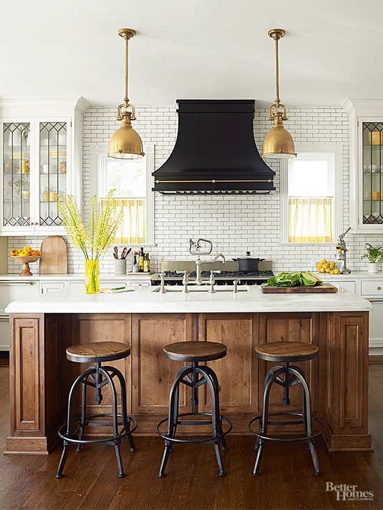 a chic vintage kitchen in white, with a stained kitchen island, a white tile backsplash and a bold black hood over the cooker