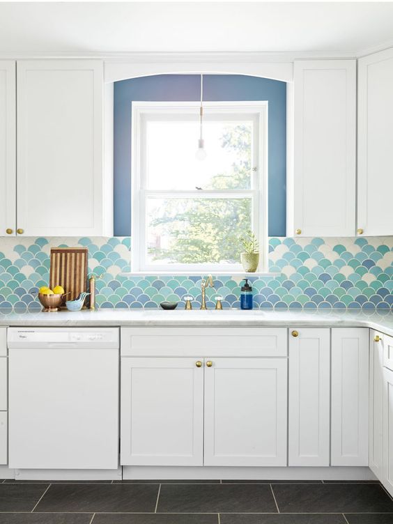 a chic white kitchen with shaker cabinets, a bold ombre blue, green and white fish scale tile backsplash and neutral countertops