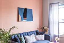 a colorful living room with a Peach Fuzz accent wall, a navy sofa, a white pouf, a pink rug and some bold artwork