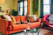 a colorful living room with chartreuse walls, an orange sofa and a pink chair, some plants and pendant lamps
