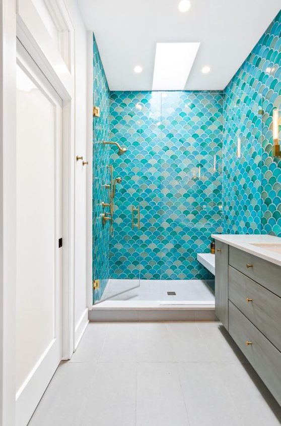 a colorful mermaid bathroom decorated with bright fishscale tiles, a wooden vanity and touches of gold is chic