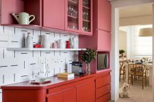 a colorful pink and red kitchen with sleek cabinets with no handles and a catchy patterned white tile backsplash