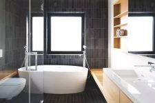 a contemporary bathroom all clad with matte dark skinny tiles and refreshed with light colored wood and white pieces