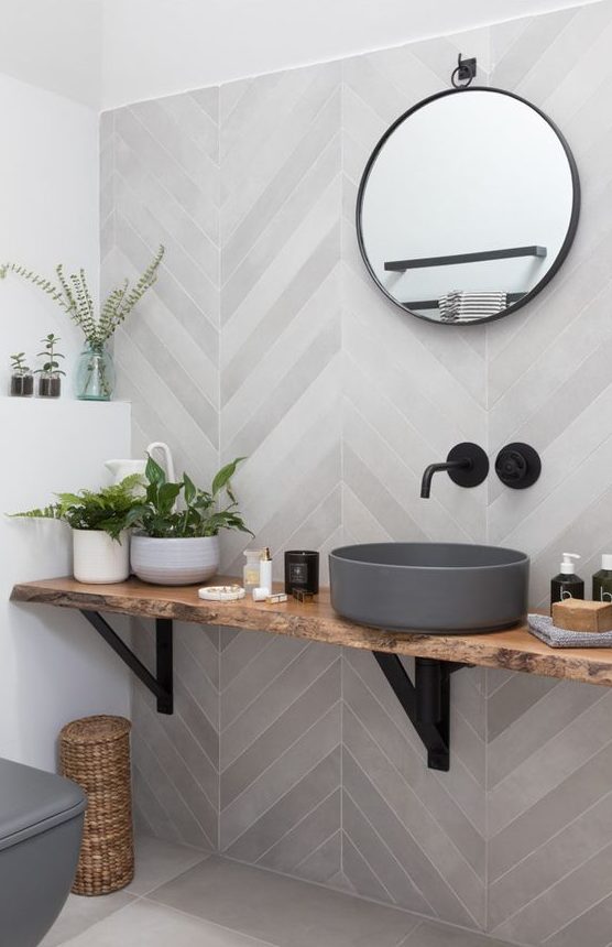 A contemporary bathroom with grey herringbone tiles, a wall mounted vanity and a concrete sink plus a round mirror