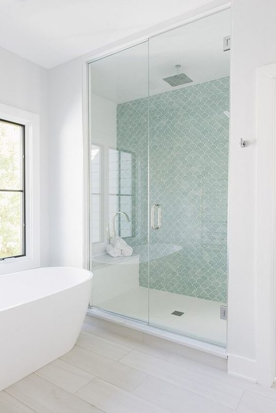 a contemporary coastal bathroom with an aqua fishscale wall, all-neutrals around and a free-standing tub by the window