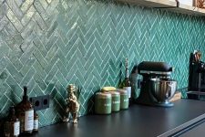 a contemporary kitchen with sleek black cabinets, an emerald herringbone tile backsplash, an open shelf with decor