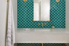 a contemporary neutral bathroom clad with green fishscale tiles, a stone vanity and a shelf and gold fixtures and lights
