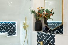 a contrasting bathroom in white, with black scallop tiles here and there, gold fixtures and a geometric mirror in a frame