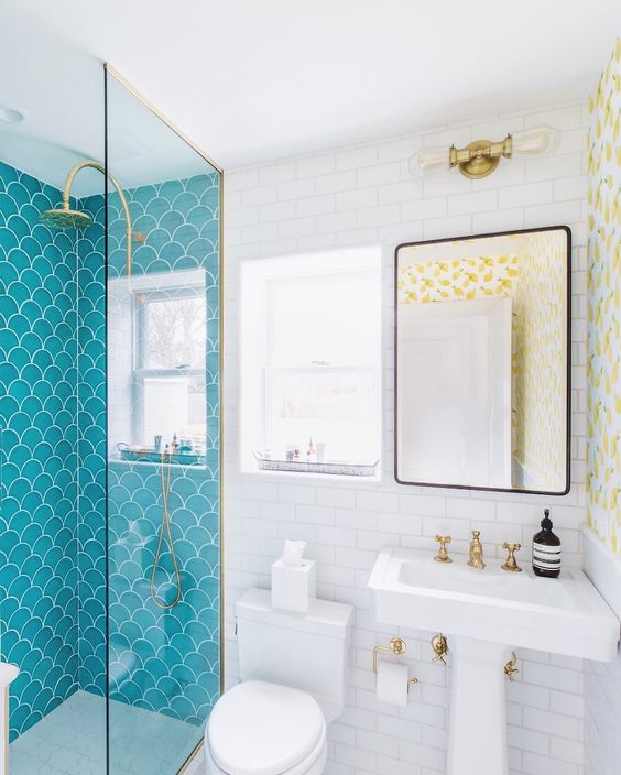 A contrasting bathroom with blue fishscale and white subway tiles, a free standing sink, a mirror and gold fixtures