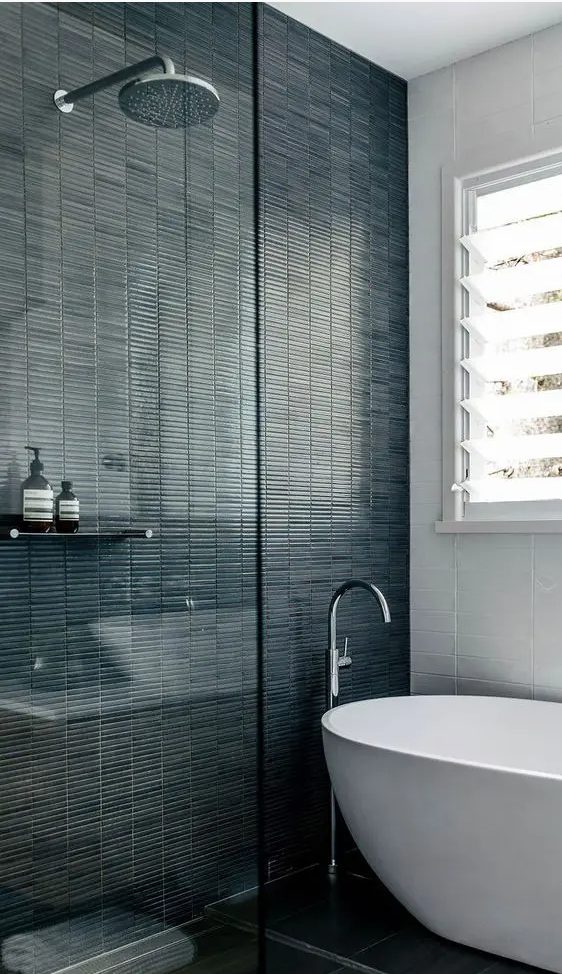 a contrasting bathroom with white stacked and dark green skinny tiles, an oval tub and a shower space