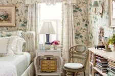 a cottage bedroom with floral wallpaper, a neutral bed with light green bedding, a white nightstand and a bookshelf