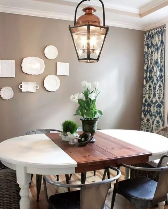 a cozy rustic dining room with taupe walls, a gallery wall of plates, an oval table, metal and woven chairs and a cool lantern