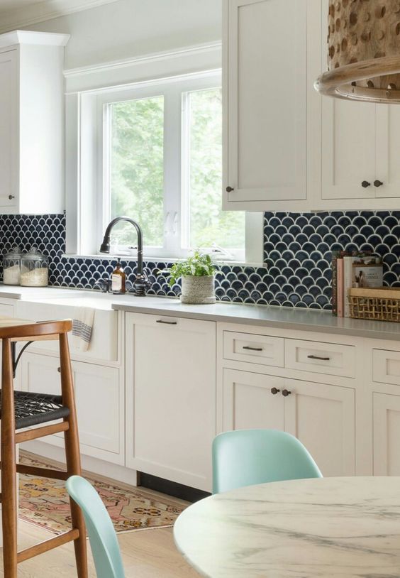a creamy farmhouse kitchen with grey countertops, a navy fih scale tile backsplash and black fixtures