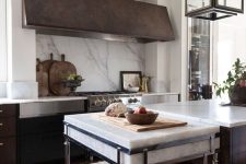 a dark-stained kitchen with white stone countertops and a backsplash plus an oversized aged metal hood is amazing