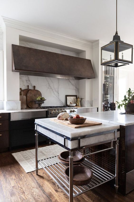A dark stained kitchen with white stone countertops and a backsplash plus an oversized aged metal hood is amazing